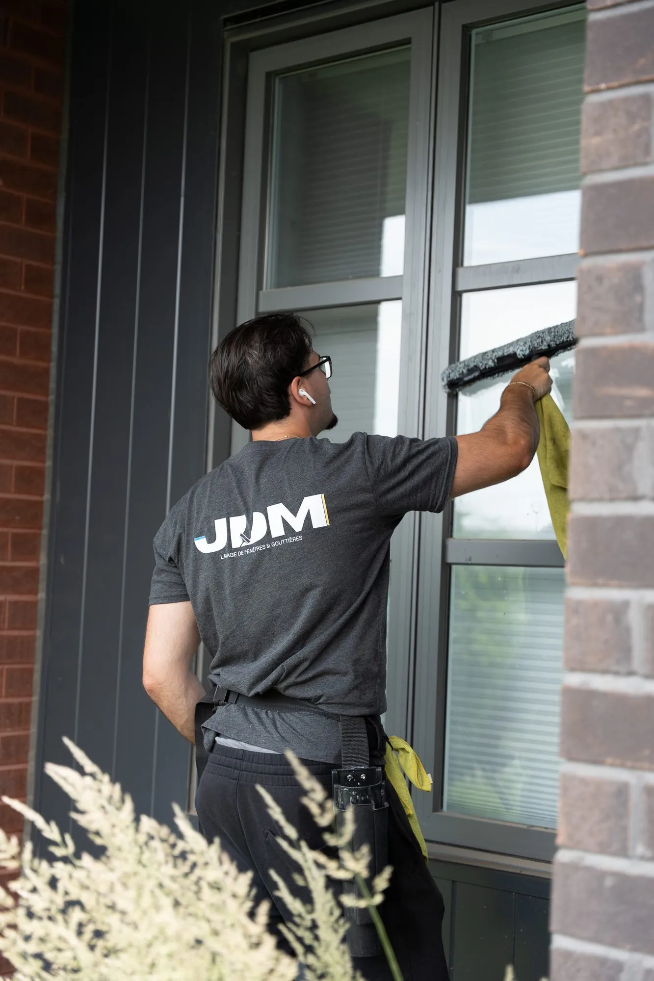 A Lavage JDM technician carefully cleans a ground-floor window beside a brick wall.