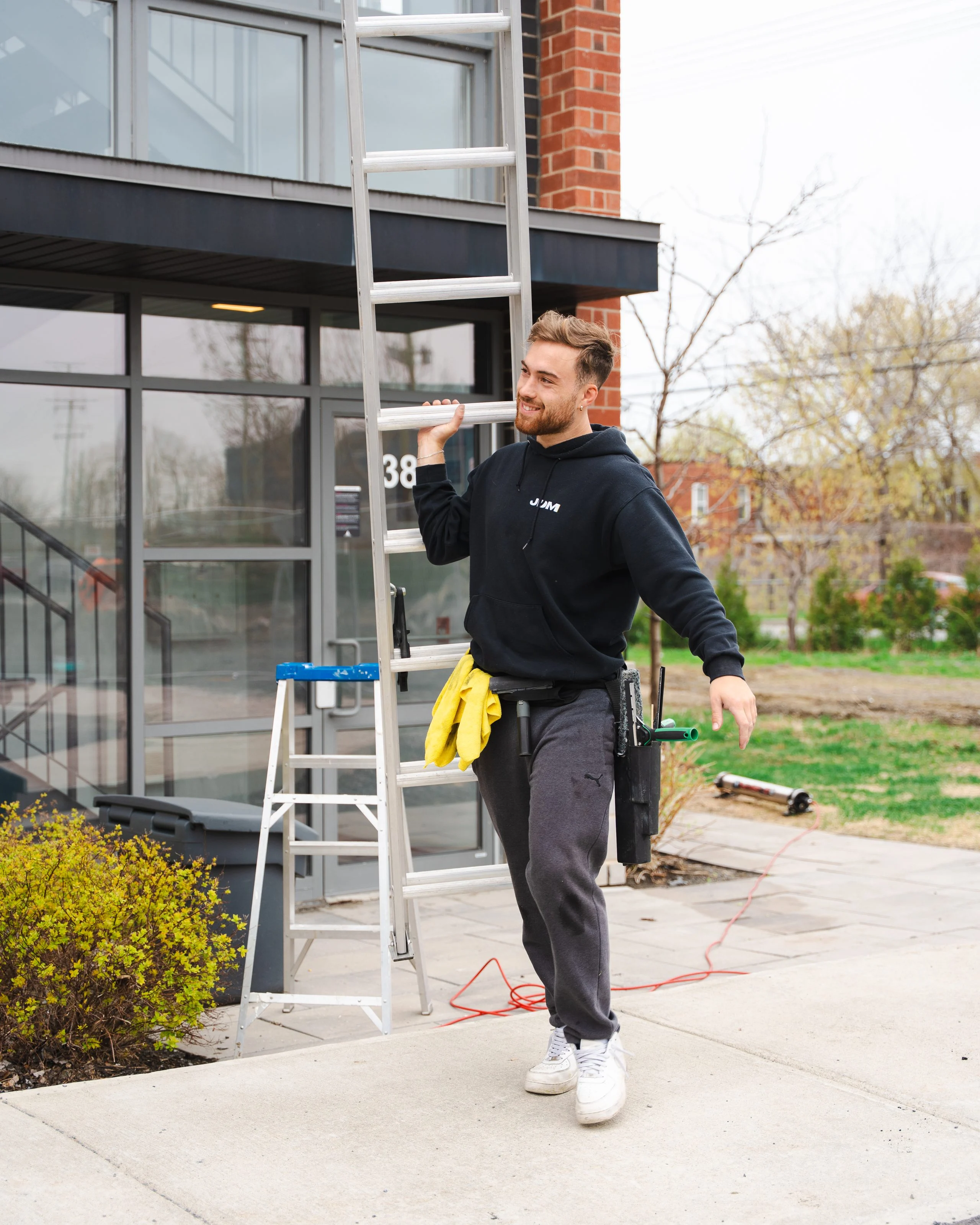 A smiling Lavage JDM technician carries a ladder beside a condominium building.