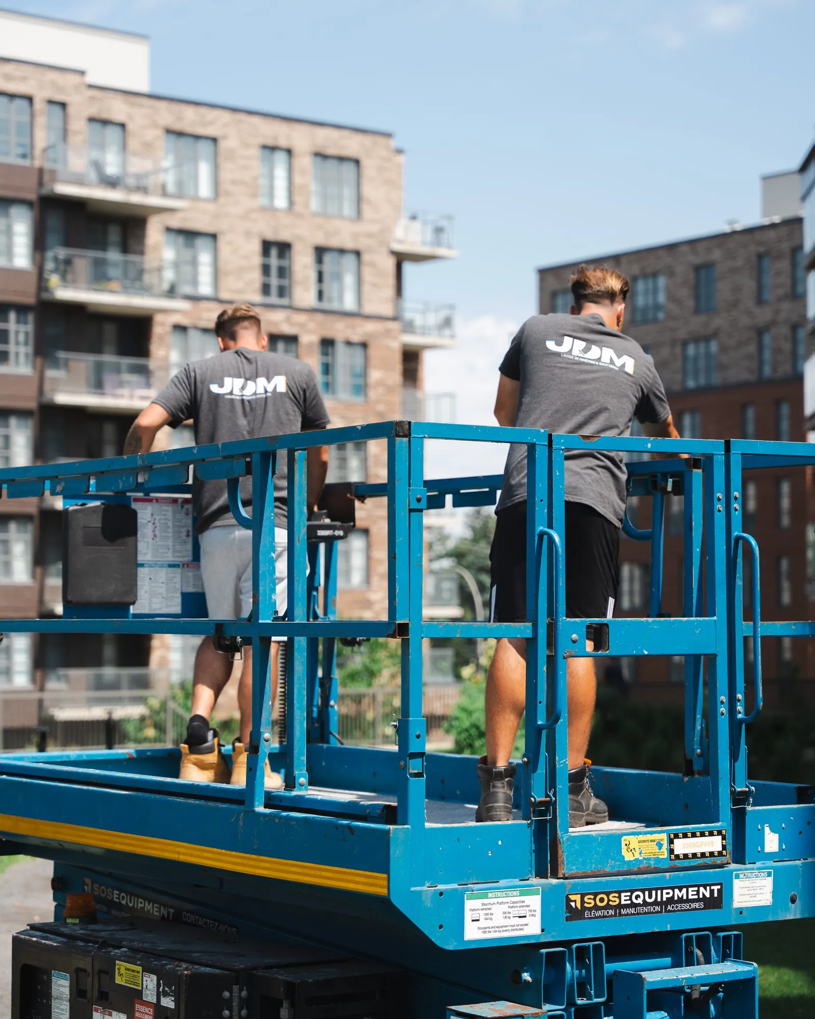 Two Lavage JDM technicians work from a scissor lift in front of the glass facade of a condominium building.