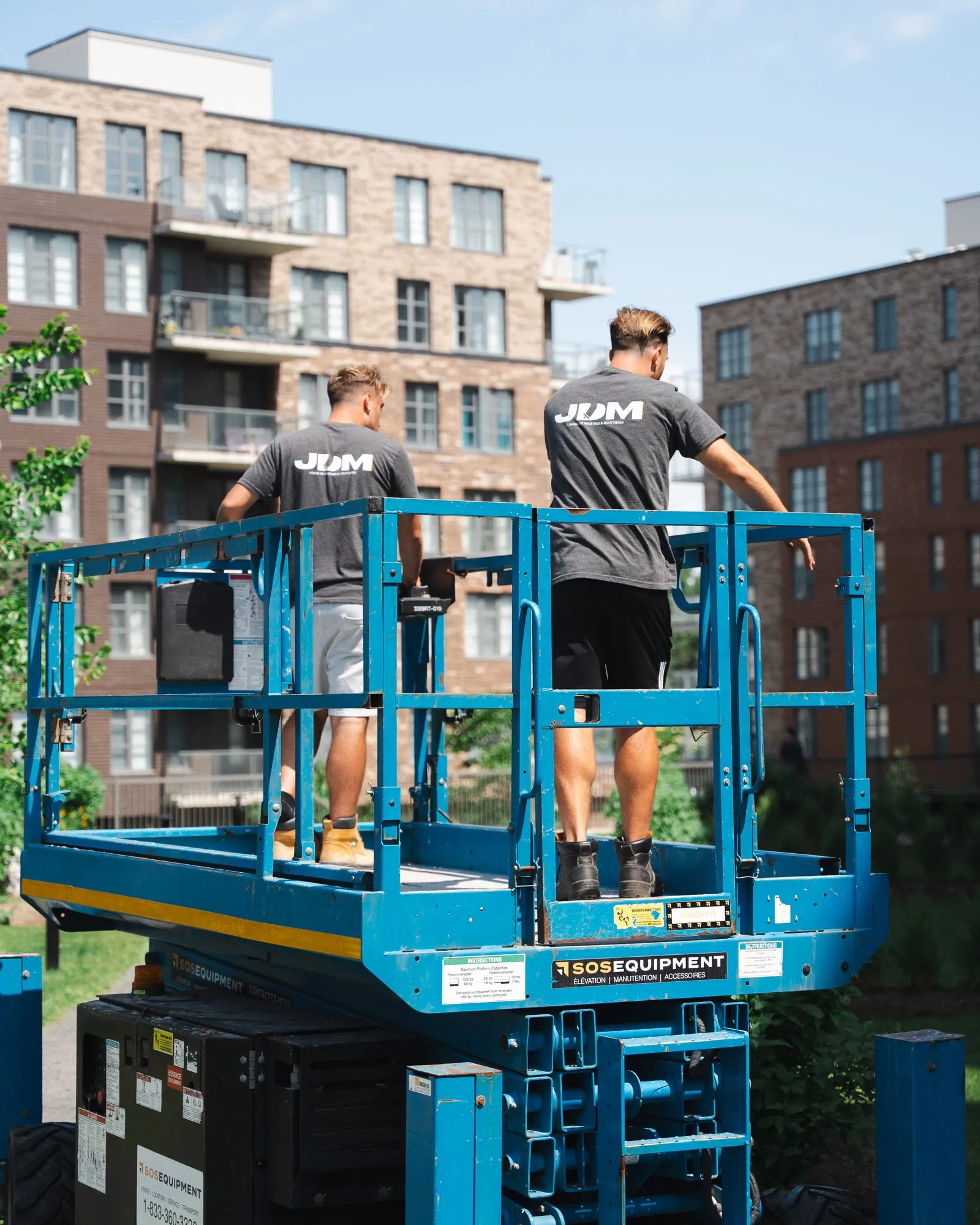 Two Lavage JDM technicians on a scissor lift in front of a condominium building.